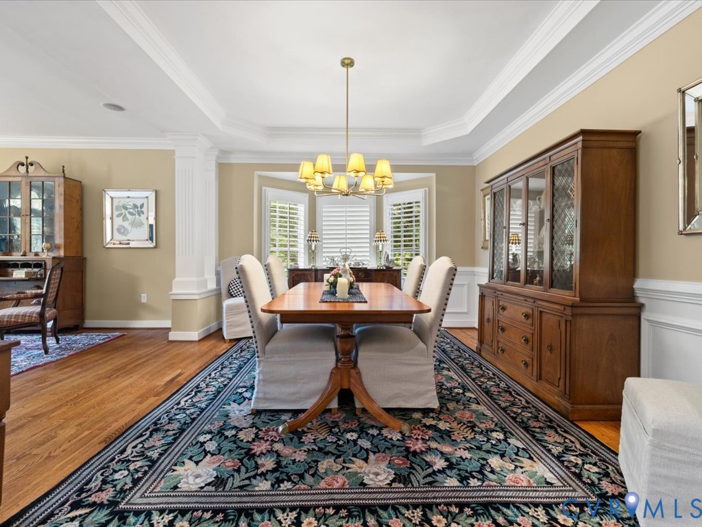 Tray ceiling featuring crown molding, hardwood flooring, and bay windows with plantation shutters