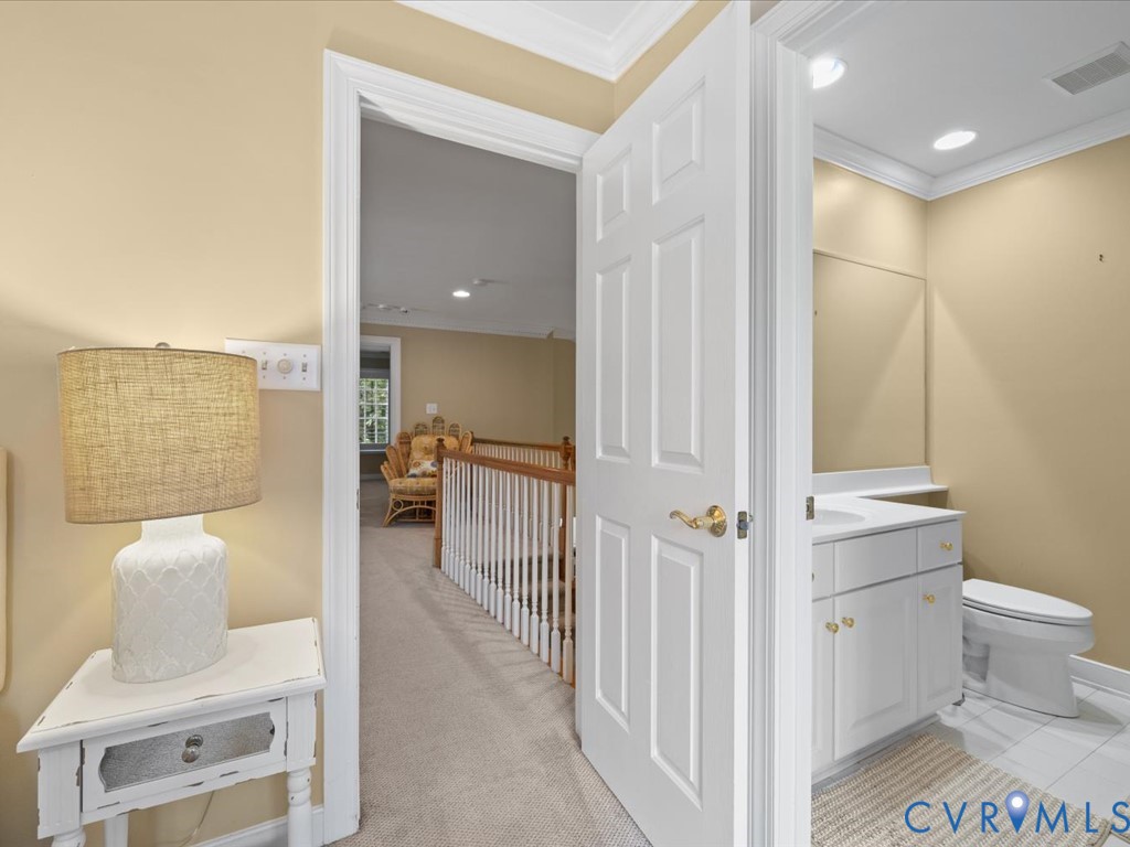 White panel door with brass hardware, white vanity with integrated sink, white toilet, and recessed lighting