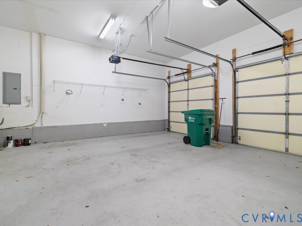 Two garage bays featuring overhead doors and track systems, concrete flooring, and fluorescent lighting