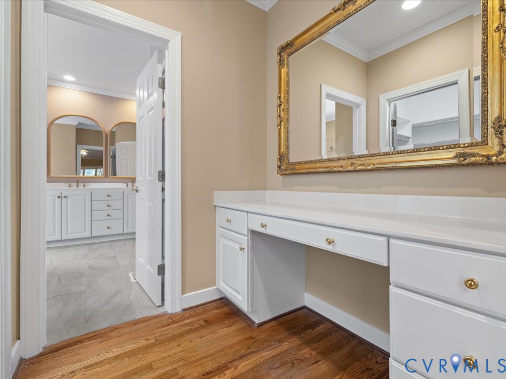 Hardwood flooring throughout, built-in vanity with white cabinetry and gold hardware, and a large ornate wall mirror