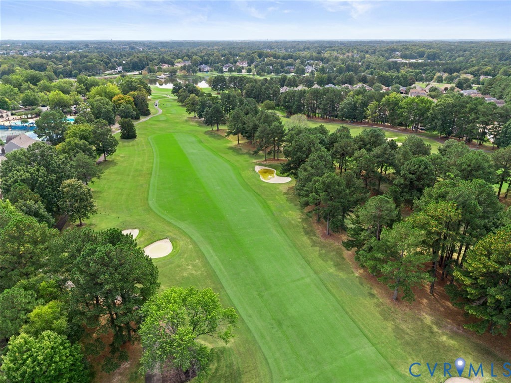 Expansive golf course fairway with manicured turf, sand traps, mature trees, and a distant body of water