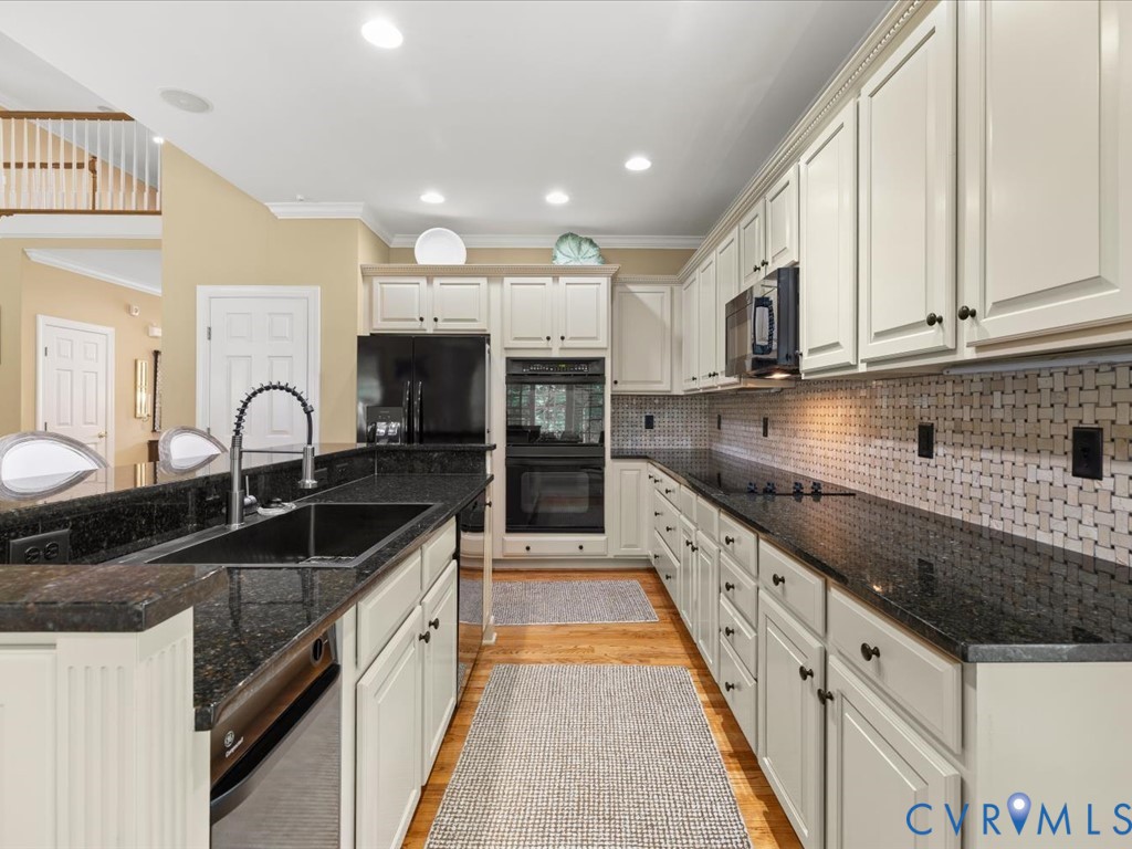 Kitchen featuring black appliances, a black sink with a gooseneck faucet, light cabinetry, dark countertops, and a patterned tile backsplash