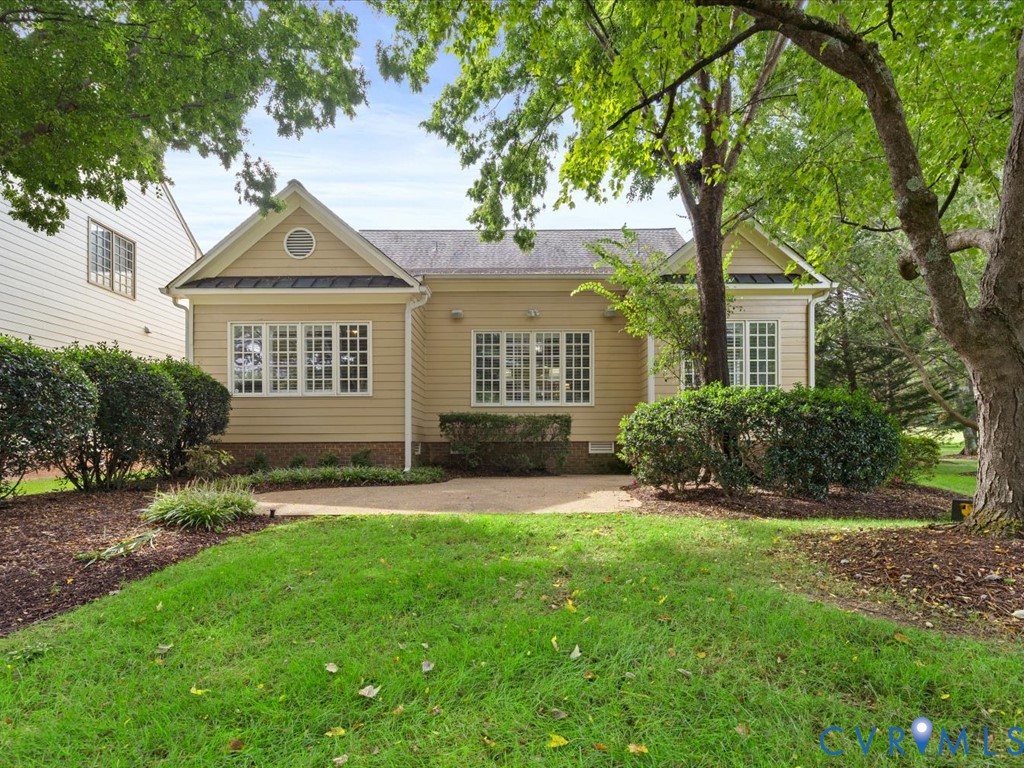 Rear exterior with light tan siding and multiple windows, surrounded by mature trees and manicured landscaping