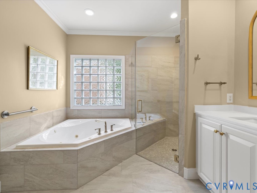 Corner jetted soaking tub, glass block window, frameless glass shower enclosure, single vanity with white cabinetry, and a light-toned tile floor