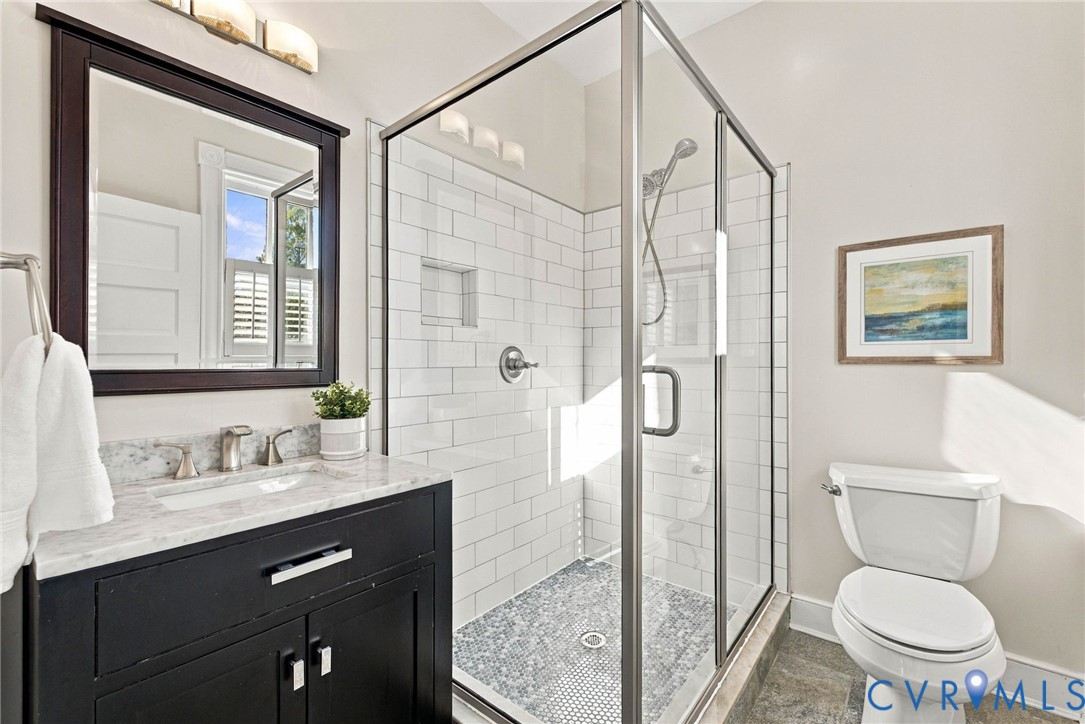 Bathroom featuring a vanity with stone-top surfacing, a walk-in shower with white subway-style wall tile and a built-in recessed niche, a framed mirror with matching dark-finish cabinetry, and a glass shower enclosure with metallic framing