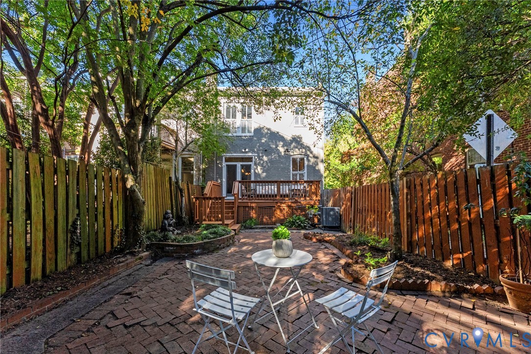 Rear exterior space featuring a raised wooden deck, a herringbone-patterned brick patio, and tall wood fencing