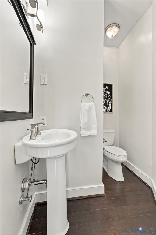 Pedestal sink with a polished chrome faucet, framed wall mirror, dual-flush toilet, and wood-finish flooring