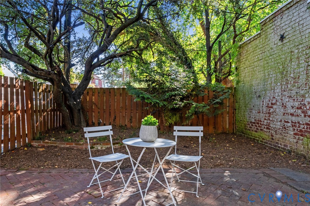 Outdoor space featuring a brick patio, vertical wood fencing, mature trees, and an exposed brick exterior wall
