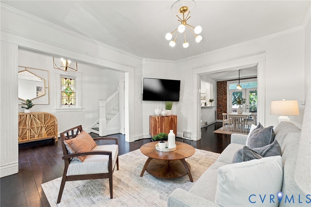 Living area featuring dark hardwood flooring, crown molding, a decorative ceiling medallion with a multi-light fixture, and a stained-glass window