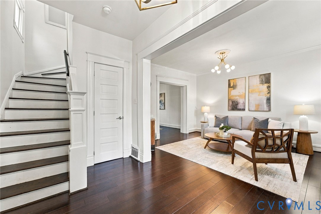 Entryway featuring wood-finish flooring, a staircase with decorative millwork, five-panel interior doors, and custom multi-arm ceiling light fixtures