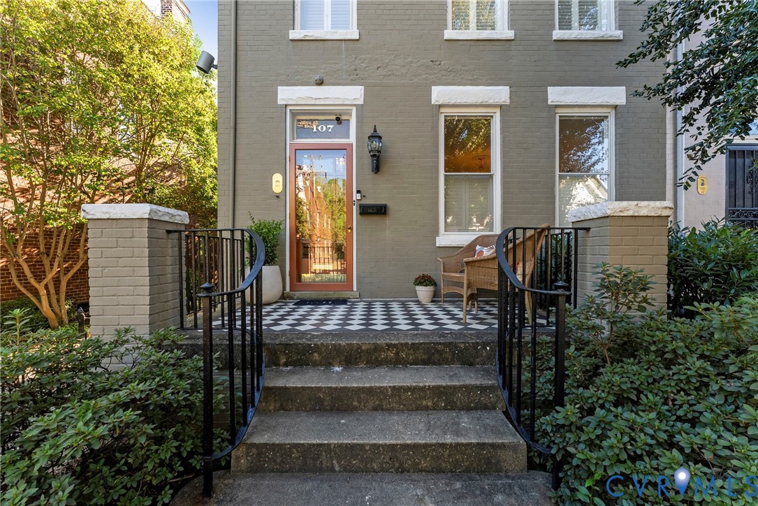 Brick exterior featuring a checkered tile porch, stone-capped brick columns, wrought-iron railings, and a multi-lite front door