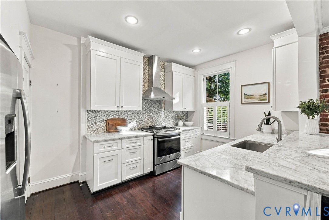 Kitchen featuring white shaker cabinetry, stone countertops, stainless steel appliances, mosaic tile backsplash, and wood-finish flooring