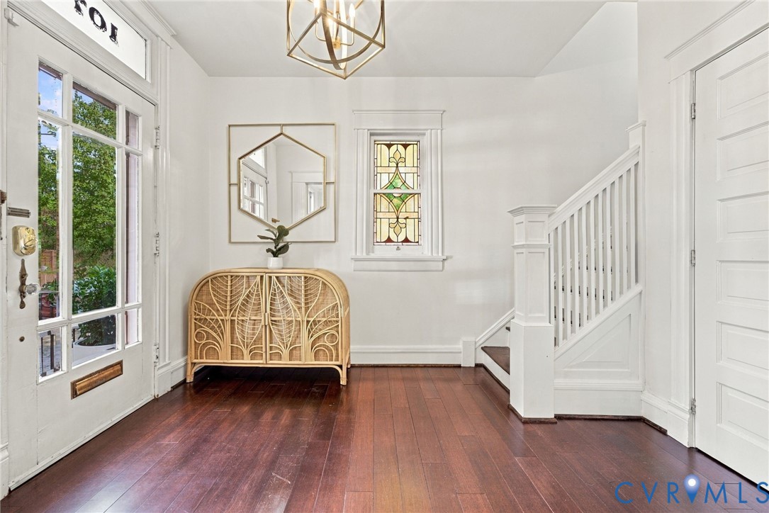 Entryway featuring dark-stained wood-finish flooring, a multi-pane glass door with an integrated transom window, a stained glass window with decorative millwork, and a geometric metal pendant light fixture