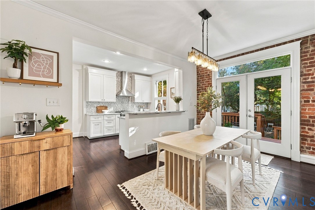 Kitchen and dining area featuring white shaker-style cabinetry, mosaic tile backsplash, wood-finish flooring, exposed brick wall, and glass-paneled double doors