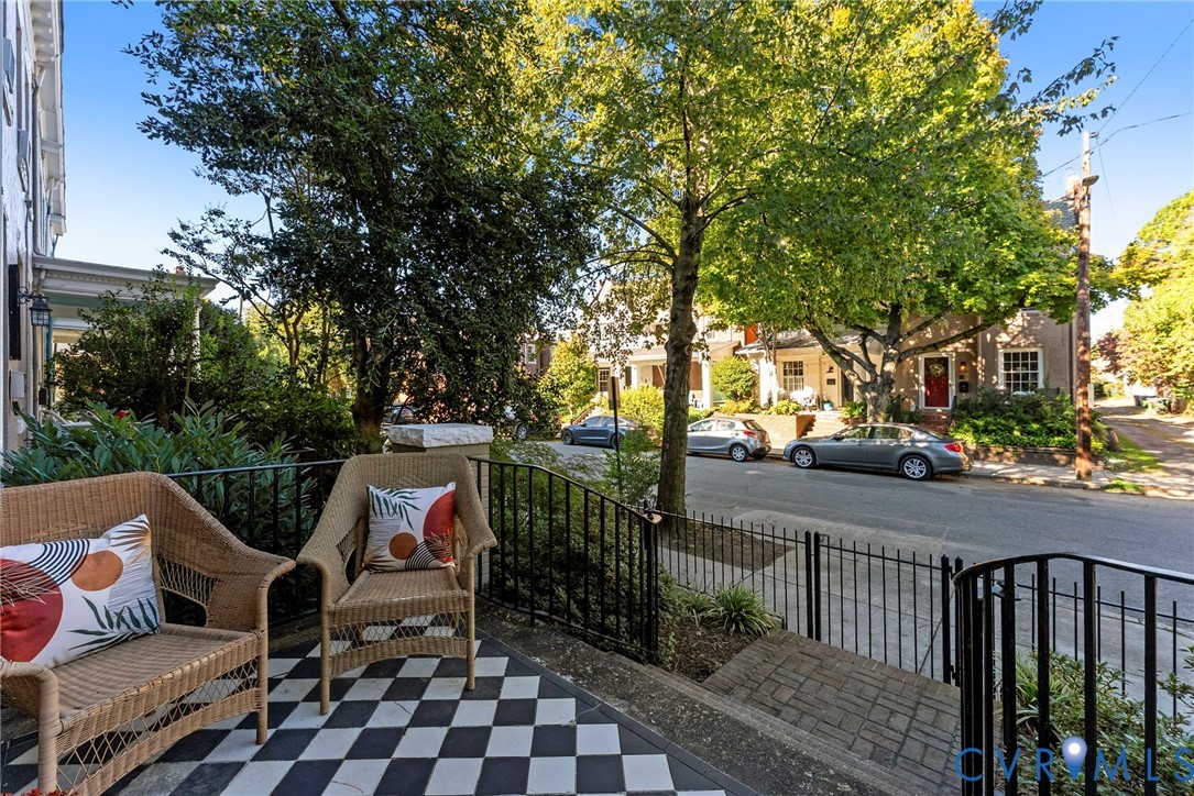 Covered front porch featuring black-and-white checkered tile flooring, wrought-iron railings, and masonry steps