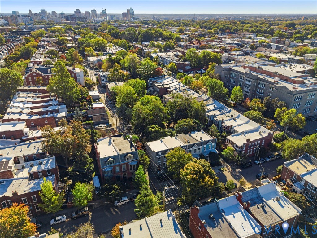 Aerial perspective of urban neighborhood featuring dense tree canopy, brick masonry architecture, flat roofing systems, and city skyline backdrop