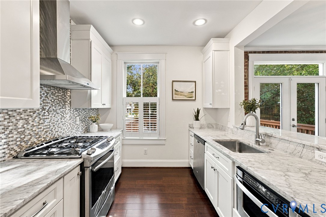 Kitchen featuring stone countertops, stainless steel appliances, a mosaic tile backsplash, custom white cabinetry, and wood-finish flooring