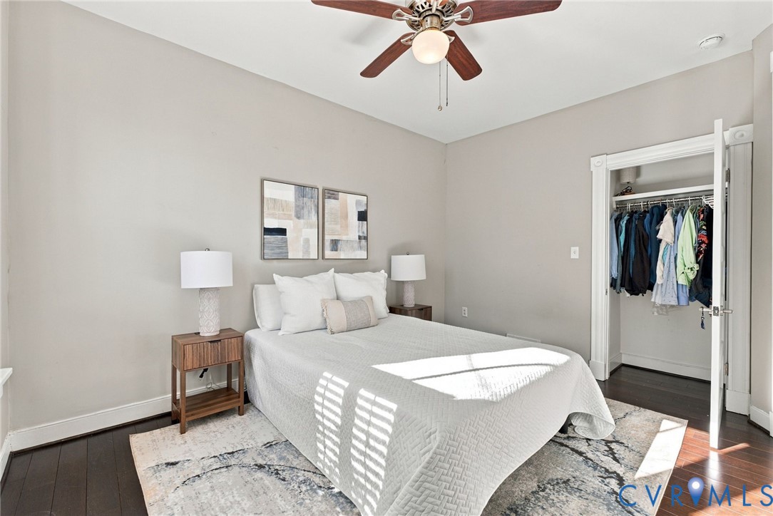Neutral-toned interior space featuring dark wood-finish flooring, a ceiling fan with light fixture, and a reach-in closet with integrated shelving