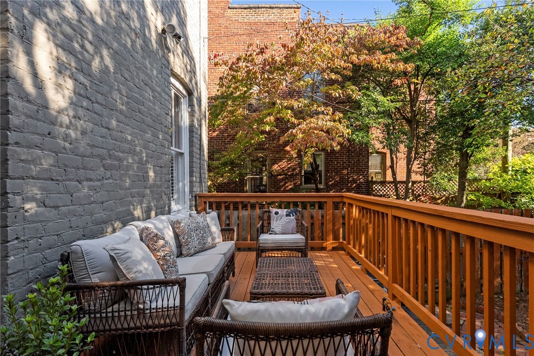 Elevated wooden deck featuring a stained finish, vertical baluster railing, painted brick exterior wall, and mature tree canopy