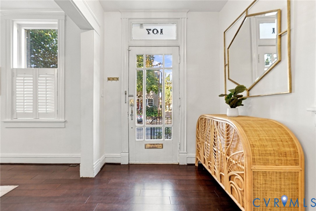 Entryway featuring wood-finish flooring, a glass-panel entry door with a transom window, and window shutters