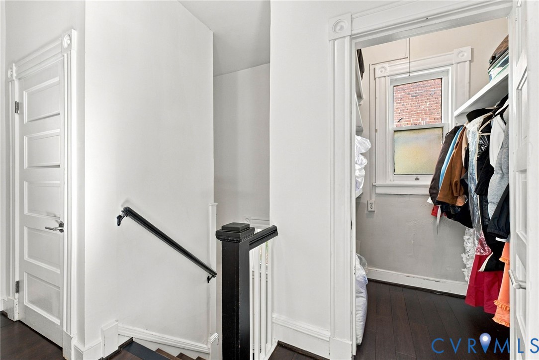 Five-panel interior doors with classic casing, dark wood-finish flooring, staircase with a custom-painted black handrail and newel post, and walk-in storage area with built-in shelving and a window
