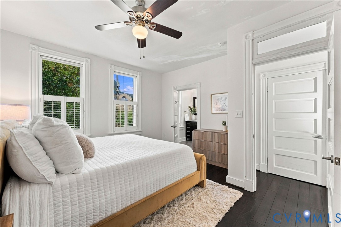 Dark wood-finish flooring, high ceilings with a central ceiling fan, classic five-panel doors, transom window, and white plantation shutters