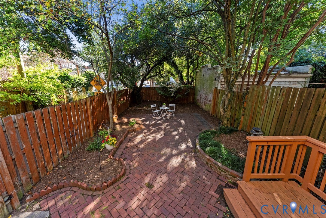 Private courtyard featuring brick herringbone paving, wood privacy fencing, mature trees, and tiered wood decking