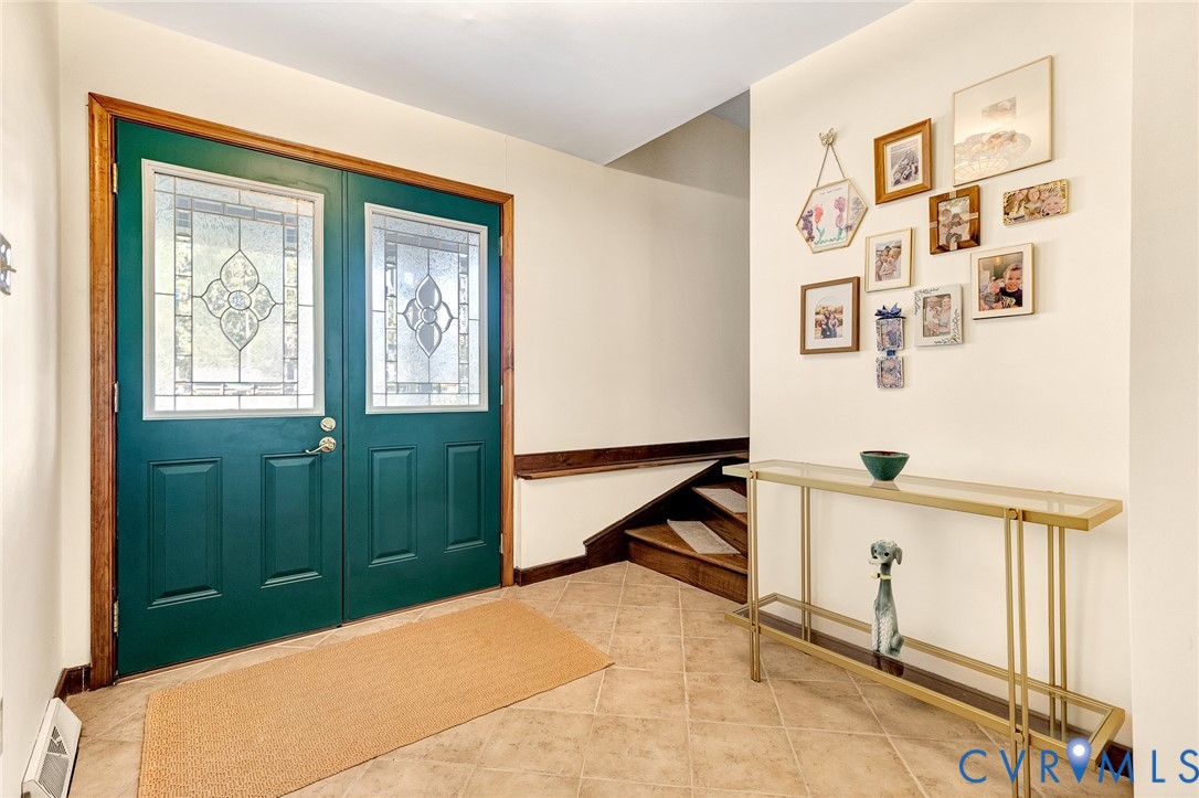 Double front doors with decorative glass inserts, tile flooring, and wood stair accents