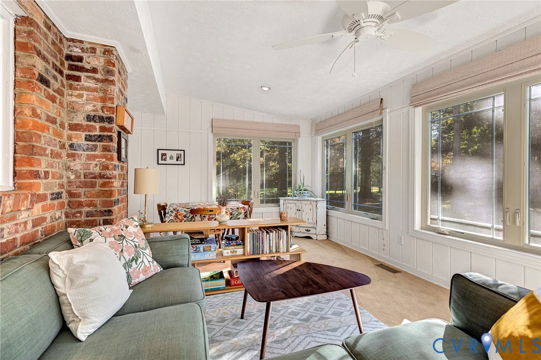 Exposed brick chimney, board and batten wall paneling, large windows, and a ceiling fan