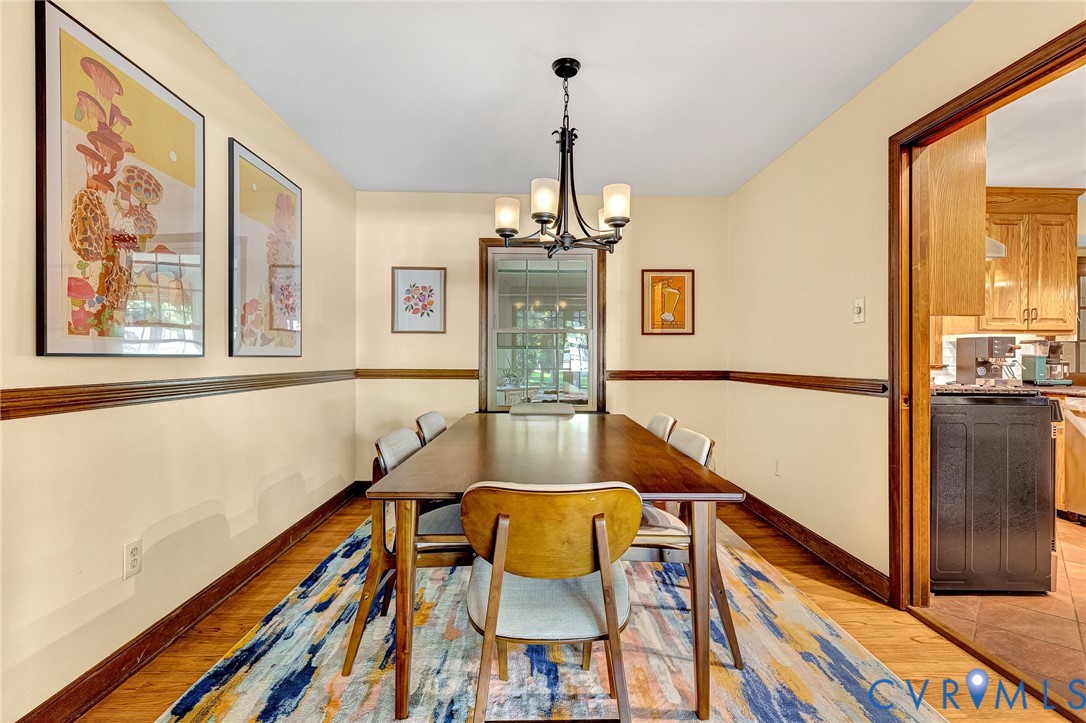 Dining space featuring wood-finish flooring, dark wood chair rail molding, a multi-arm metal chandelier, and a single-hung window with muntins