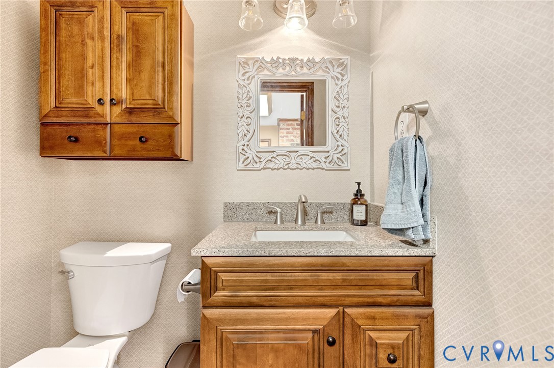 Wood-finish cabinetry, neutral stone-composite countertop with an integrated rectangular sink, three-light fixture, and textured wall finish