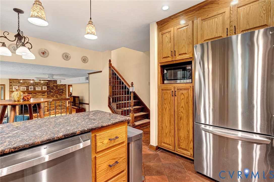 Kitchen area featuring floor-to-ceiling wood cabinetry, stainless steel appliances, stone-finish countertops, tile flooring, and decorative hanging light fixtures