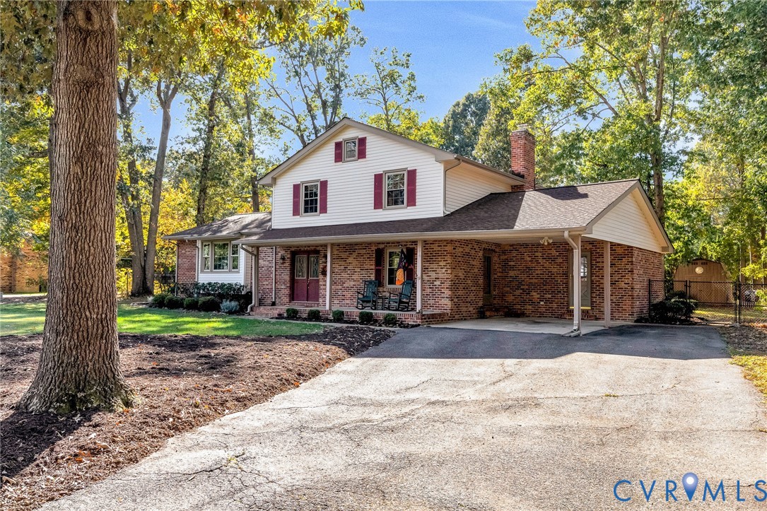 Two-story residence featuring a partial brick and siding exterior, front covered porch, attached carport, and a paved driveway