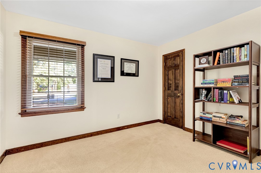 Room featuring neutral wall-to-wall carpeting, wood-trimmed windows with horizontal blinds, and a six-panel wood door