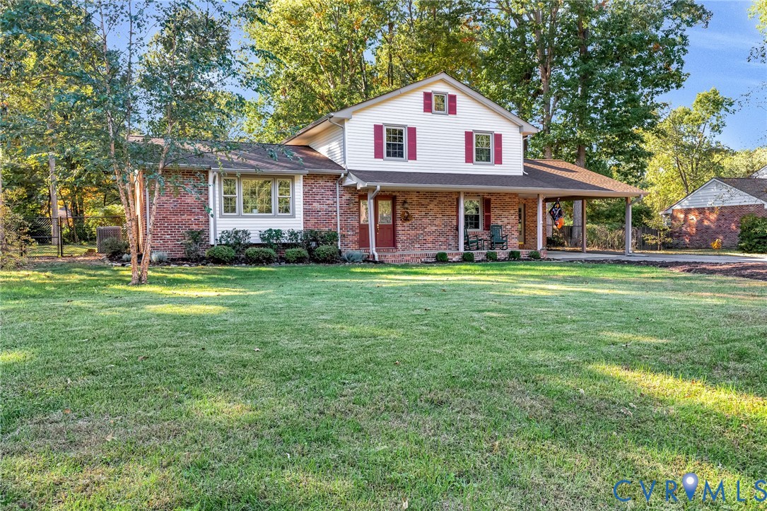 Two-story residence featuring a brick and white siding exterior, covered front porch, attached carport, and mature landscaping