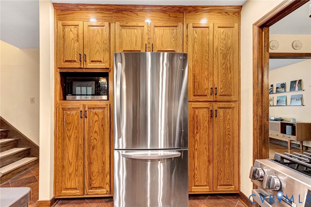 Floor-to-ceiling oak cabinetry, stainless steel refrigerator, built-in microwave, and tile flooring