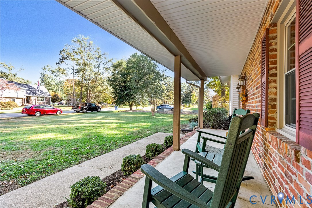Covered front porch featuring a brick exterior, red louvered shutters, concrete flooring, and decorative wall-mounted lanterns