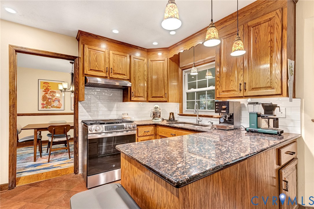 Kitchen featuring wood cabinetry, stone countertops, subway tile backsplash, stainless steel range with overhead hood, and three pendant lights