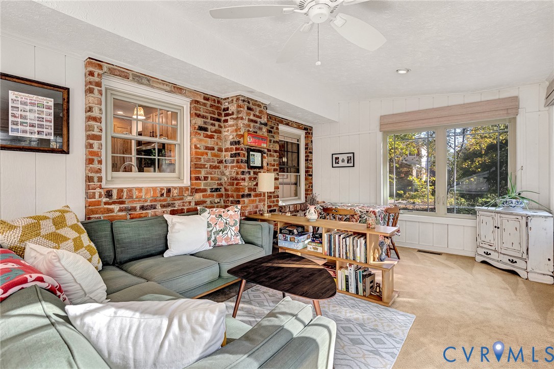 Interior space featuring an exposed brick accent wall, large picture windows, vertical wall paneling, and a ceiling-mounted fan