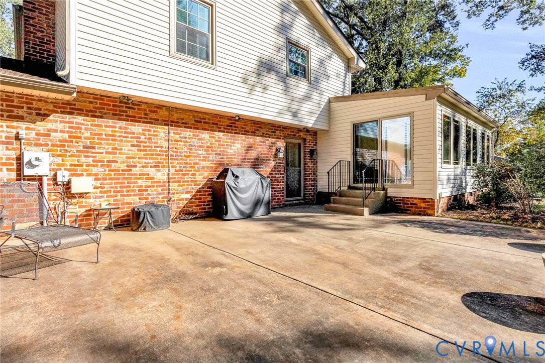 Exterior facade featuring a combination of red brick and horizontal siding, concrete patio, sliding glass door, and metal handrails