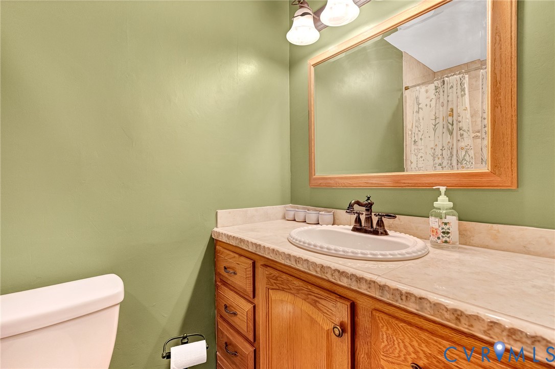 Bathroom vanity featuring wooden cabinetry, an integrated stone-finish countertop with a drop-in sink, oil-rubbed bronze faucet, and a large framed wall mirror