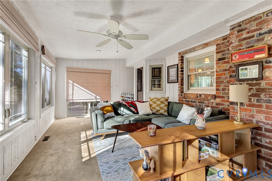 Sunroom featuring floor-to-ceiling windows, exposed brick accent wall, white vertical paneling, and a ceiling-mounted fan