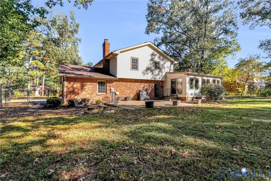 Exterior elevation featuring brick and light-colored siding, masonry chimney, concrete rear patio, and mature trees on a level lot