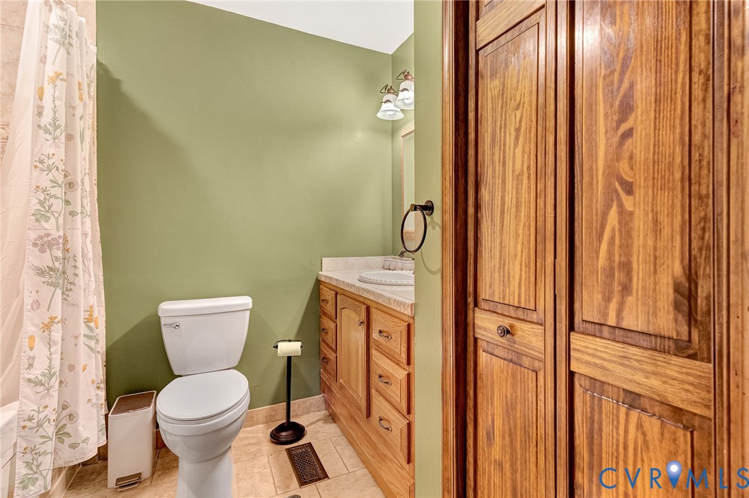 Bathroom featuring wood-finish cabinetry, stone-patterned countertop, tile flooring, and bi-fold wooden closet doors
