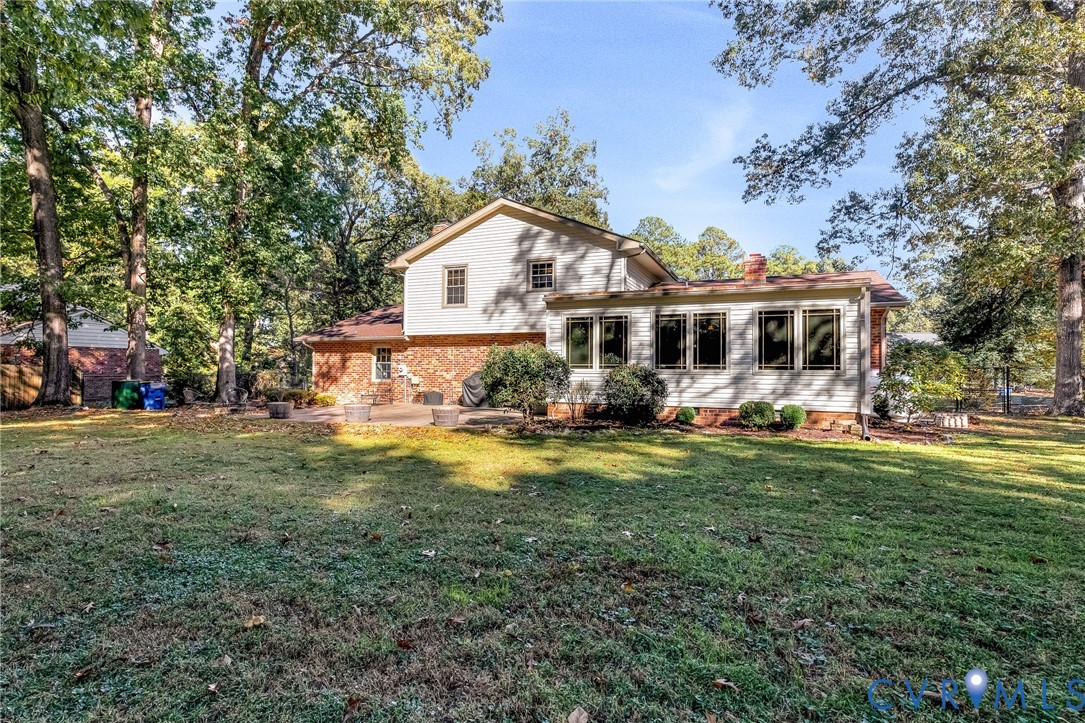 Expansive backyard featuring a manicured lawn, mature trees, multi-tone brick and horizontal siding exterior, and a stone-paver patio