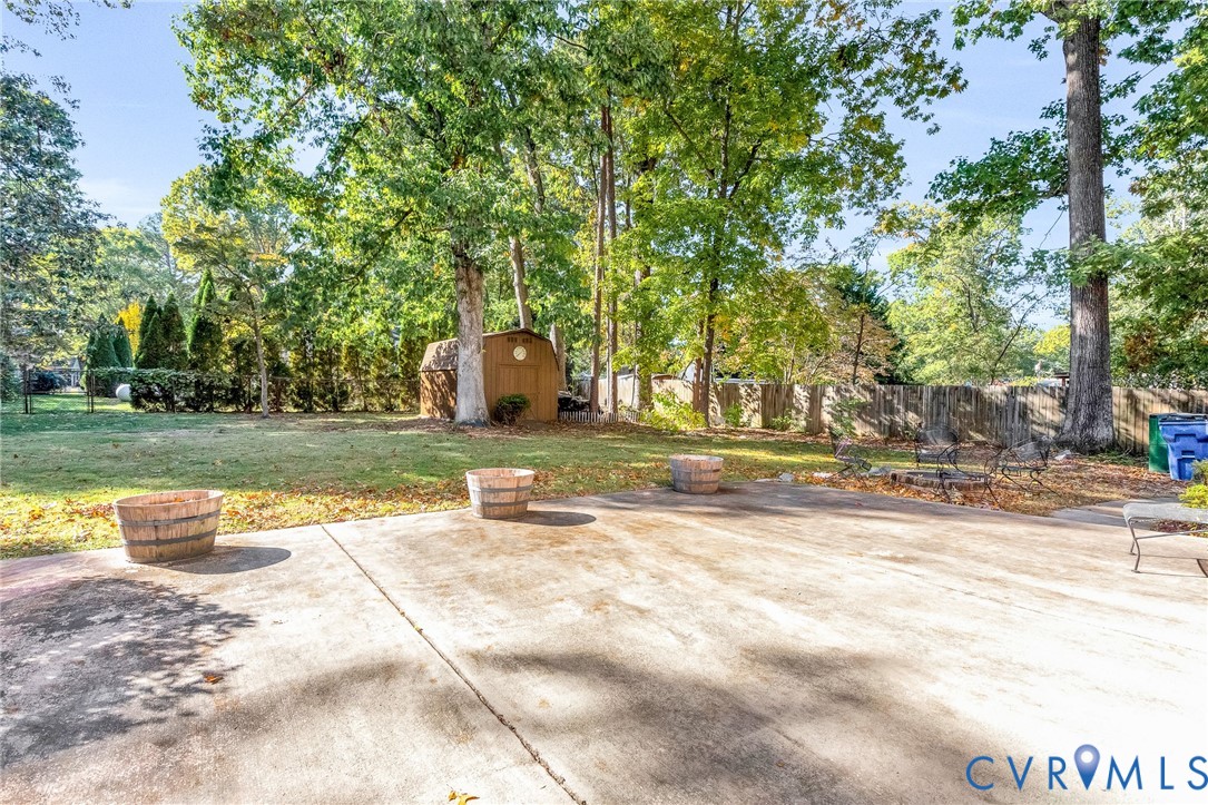 Expansive backyard featuring a concrete patio, mature trees, and a detached storage shed enclosed by wood fencing