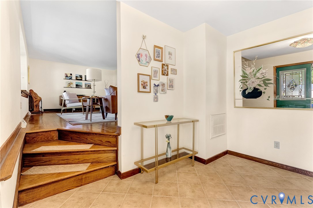 Entryway featuring ceramic tile flooring, a built-in recessed mirror, a curved wooden staircase with integrated steps, and a decorative front door with leaded glass inlay