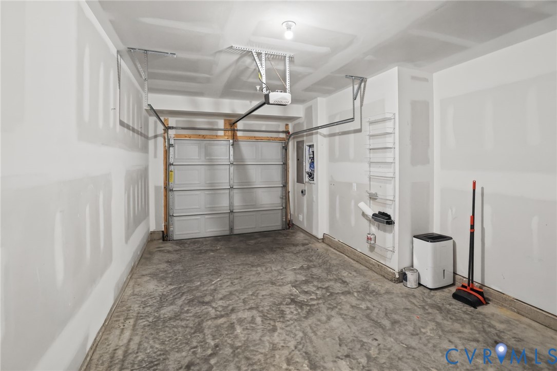 Single-car garage featuring a concrete floor, finished drywall, an overhead sectional garage door, and a built-in wall-mounted shelving unit