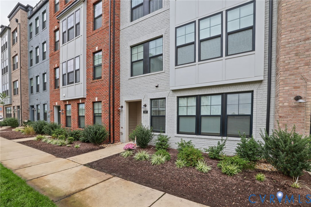 Modern multi-story exterior featuring painted brick masonry, prominent bay windows, dark window frames, and exterior wall-mounted lighting