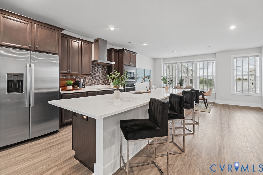 Kitchen featuring dark wood cabinetry, a central island with a stone countertop, a tile backsplash, stainless steel appliances, and wood-finish flooring